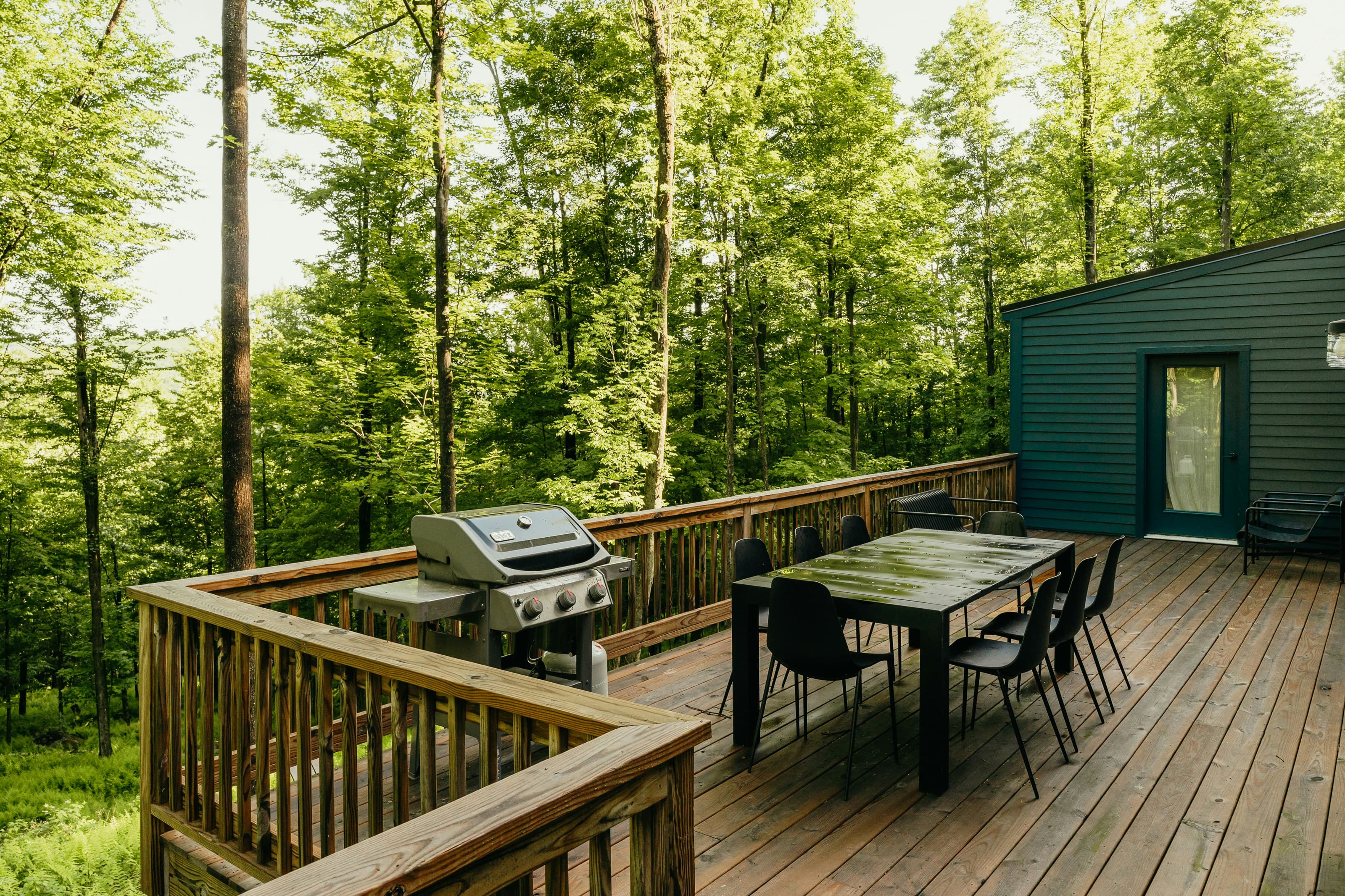 A modern wood deck with a dining table, surrounded by trees